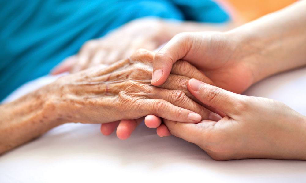 close-up of white young female caregiver holding hand of white elderly female